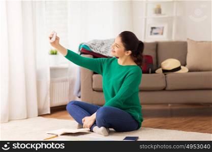 vacation, tourism, travel and people concept - happy young woman with smartphone going on trip and taking selfie at home. woman with smartphone taking selfie at home