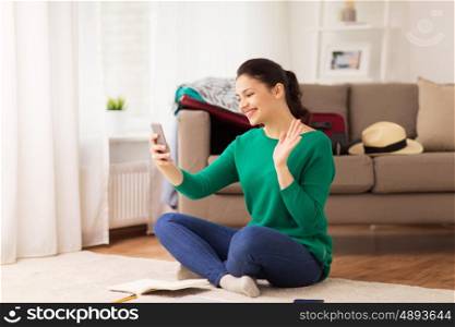 vacation, tourism, travel and people concept - happy young woman with smartphone waving hand at home