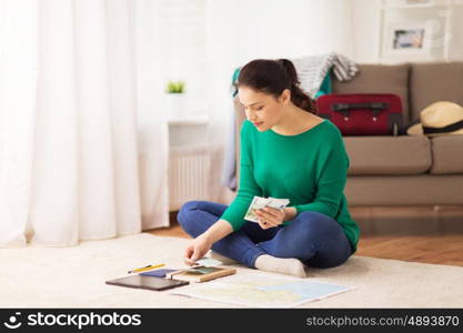 vacation, tourism, travel, finances and people concept - happy young woman with money, tablet pc computer and map at home