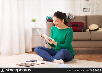 vacation, tourism, travel, finances and people concept - happy young woman with money, tablet pc computer and map at home