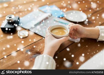 vacation, tourism, winter holidays and people concept - hands with coffee cup and travel stuff over snow