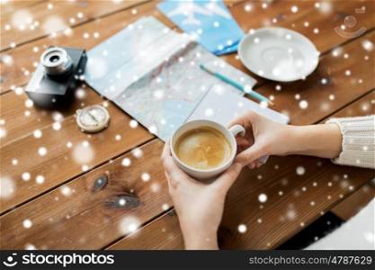 vacation, tourism, winter holidays and people concept - hands with coffee cup and travel stuff over snow