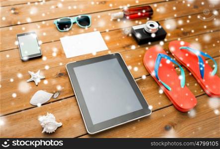 vacation, tourism, winter holidays, technology and travel concept - tablet pc computer and beach stuff over snow