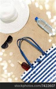 vacation, travel and summer concept - beach bag, sunscreen, sunglasses and hat on sand. beach bag, sunscreen, sunglasses and hat on sand