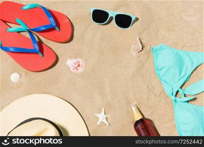 vacation, travel and summer holidays concept - straw hat, flip flops, sunglasses and sunscreen oil with seashells on beach sand. straw hat, flip flops and sunglasses on beach sand