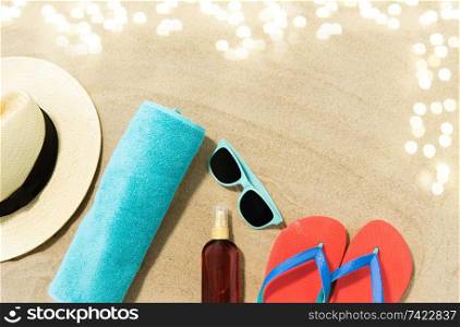 vacation, travel and summer holidays concept - straw hat, flip flops, sunglasses and sunscreen oil with seashells on beach sand. straw hat, flip flops and sunglasses on beach sand