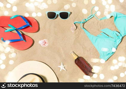 vacation, travel and summer holidays concept - straw hat, flip flops, sunglasses and sunscreen oil with seashells on beach sand. straw hat, flip flops and sunglasses on beach sand