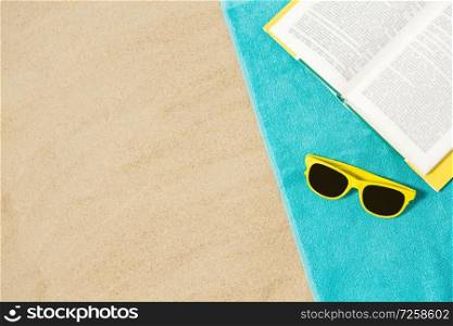 vacation, travel and summer holidays concept - yellow sunglasses and book on blue beach towel on sand. sunglasses and book on beach towel on sand