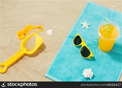 vacation, travel and summer holidays concept - yellow sunglasses, sand toys, seashells and juice drink on beach towel. sunglasses, sand toys and juice on beach towel