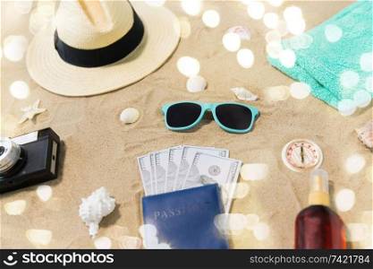 vacation, travel and tourism concept - vintage camera, money in passport, hat and sunglasses on beach sand. money in passport, shades and hat on beach sand