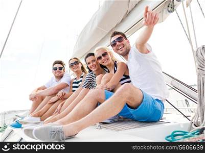 vacation, travel, sea, friendship and people concept - smiling friends sitting on yacht deck and pointing finger