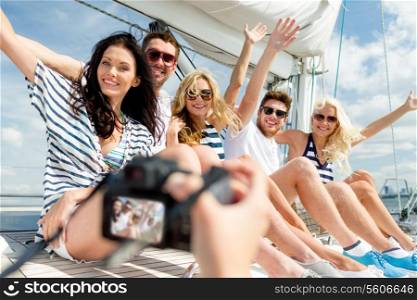 vacation, travel, sea, friendship and people concept - smiling friends sitting on yacht deck and photographing