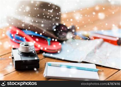 vacation, travel, tourism and winter holidays concept - close up of camera, notebook with pencil and personal accessories over snow
