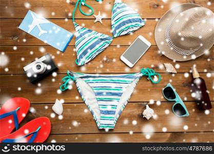 vacation, travel, tourism and winter holidays concept - smartphone, camera and beach stuff over snow