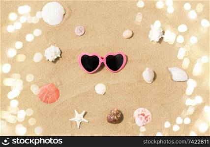 vacation, valentine’s day and summer holidays concept - pink heart-shaped sunglasses and shells on beach sand. heart-shaped sunglasses and shells on beach sand