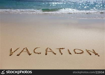 Vacation written in the sand on the beach, blue waves on background