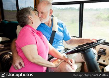 Vacationing senior couple kissing while he is driving their motor home.