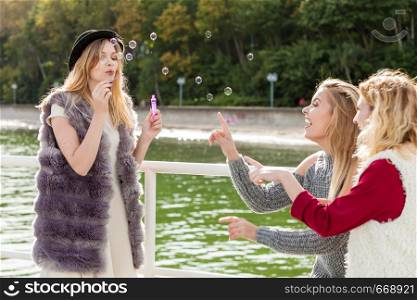 Vacations joy, friendship concept. Women friends having fun blowing soap bubbles outdoor.. Women playing together blowing soap bubbles