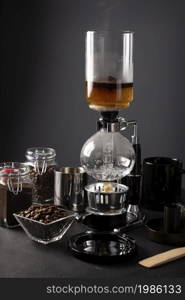 Vacuum coffee maker also known as vac pot, siphon or syphon coffee maker and toasted coffee beans on rustic black stone table.