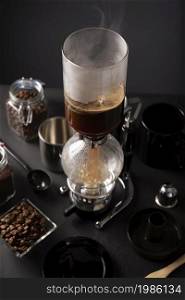 Vacuum coffee maker also known as vac pot, siphon or syphon coffee maker and toasted coffee beans on rustic black stone table.