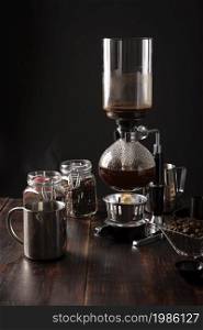 Vacuum coffee maker also known as vac pot, siphon or syphon coffee maker. Metallic cup and toasted coffee beans on rustic wooden table