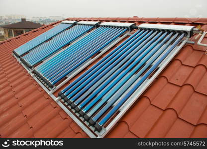 Vacuum collectors- solar water heating system on red roof of the house.