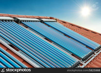 Vacuum collectors- solar water heating system on red roof of the house under shining sun and blue sky