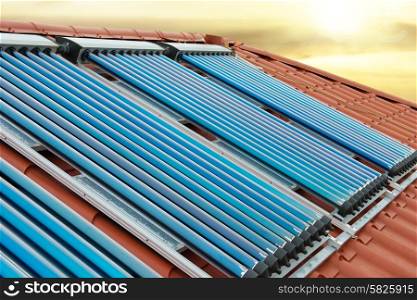 Vacuum collectors- solar water heating system on red roof of the house under shining sun