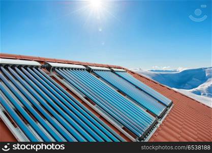 Vacuum collectors - solar water heating tubes. Vacuum collectors - solar water heating tubes on roof of the house with sun and snow mountains