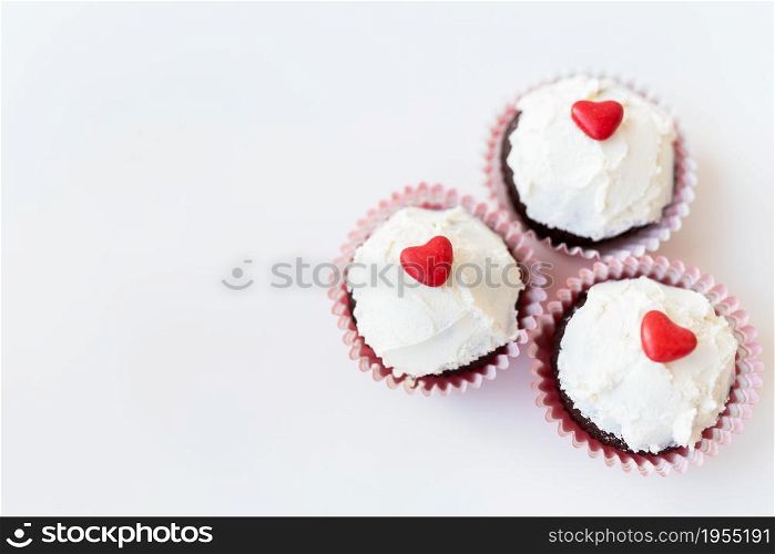 Valentine-14 February. Sweet chocolate muffins with butter cream and a red heart for decoration on a white background. Valentine-14 February. Sweet chocolate muffins with butter cream and a red heart for decoration on a white background.