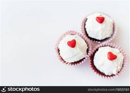 Valentine-14 February. Sweet chocolate muffins with butter cream and a red heart for decoration on a white background. Valentine-14 February. Sweet chocolate muffins with butter cream and a red heart for decoration on a white background.