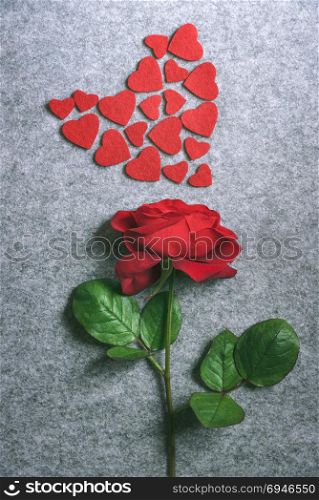 Valentine day image with a beautiful red rose and small red fabric hearts displayed in a shape of a big heart, on a vintage grey fabric background.