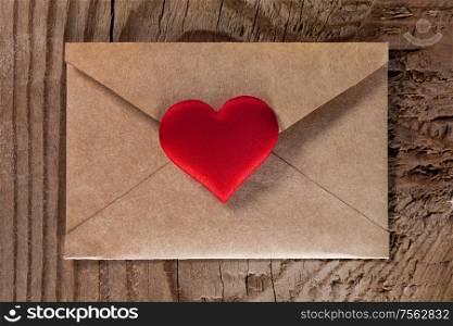 Valentine day love letter, envelope of craft paper with red heart on wooden background. Valentine day love letter