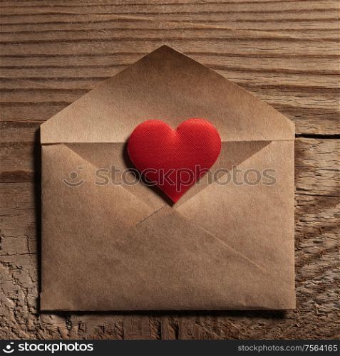 Valentine day love letter, envelope of craft paper with red heart on wooden background. Valentine day love letter