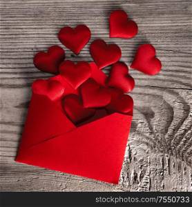 Valentine day love letter, envelope of craft red paper with red hearts heap spread on wood background.. Valentine day love letter