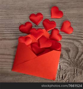 Valentine day love letter, envelope of craft red paper with red hearts heap spread on wood background.. Valentine day love letter