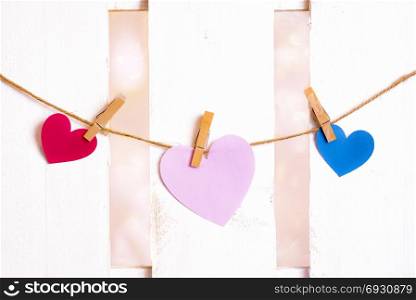 Valentine day theme image with one big pink heart in the middle, one red and one blue on the sides, made from paper and tied to a string with wooden clips.