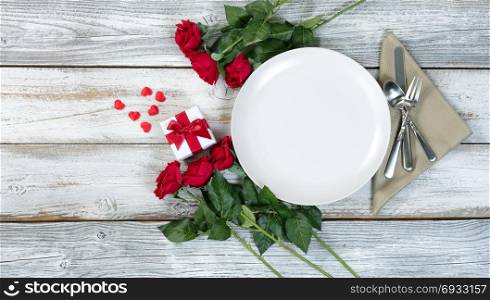 Valentine dinner setting with gift, red roses and heart shapes on rustic table