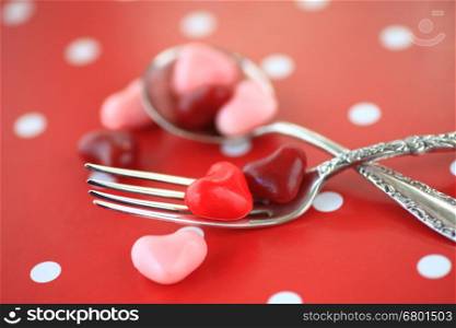 Valentine heart candies on silverware on a red and white polka dot background