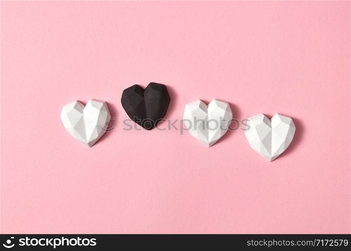 Valentine&rsquo;s creative composition from gypsum white hearts and one is black on a light pink background, copy space. Greeting card.. Holiday pattern with plaster small hearts.