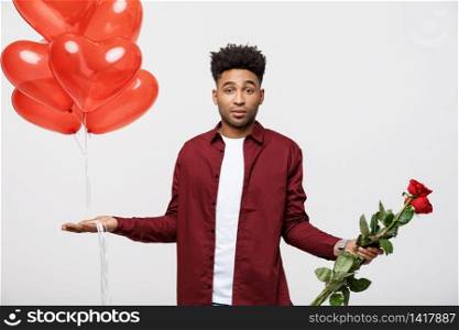 Valentine&rsquo;s Day: African American man holding red rose and balloon with disappointed expression. Valentine&rsquo;s Day: African American man holding red rose and balloon with disappointed expression.