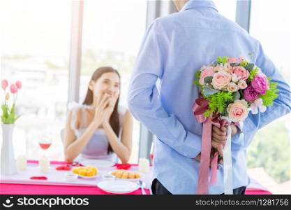 Valentine&rsquo;s day and asian Young happy couple concept,Close up of asian a man holding a bouquet of roses woman with hands over her face awaits surprise after lunch In a restaurant background