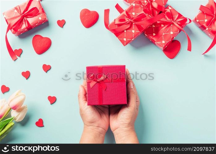 Valentine&rsquo;s day and birthday. Woman hands holding gift or present box decorated and red heart surprise on blue background, Female&rsquo;s hand hold gift box package in craft paper Top view flat lay