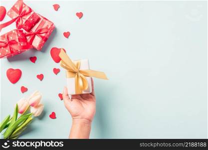 Valentine&rsquo;s day and birthday. Woman hands holding gift or present box decorated and red heart surprise on blue background, Female&rsquo;s hand hold gift box package in craft paper Top view flat lay