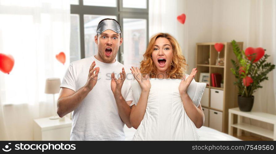 valentine&rsquo;s day and people concept - scared couple in white t-shirts with eye sleeping mask over home bedroom decorated with heart shaped balloons background. scared couple with eye sleeping mask and pillow