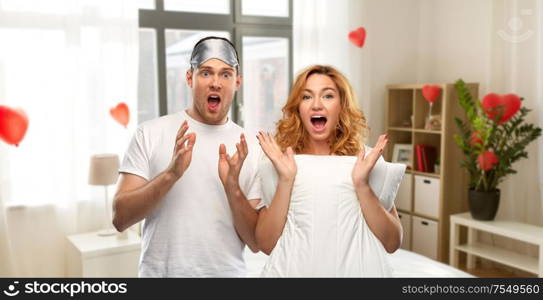 valentine&rsquo;s day and people concept - scared couple in white t-shirts with eye sleeping mask over home bedroom decorated with heart shaped balloons background. scared couple with eye sleeping mask and pillow