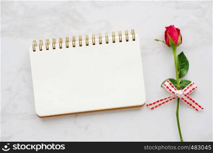 Valentine's day background, template, Red rose and blank notebook paper on white marble background with copy space for text, top view, flat lay