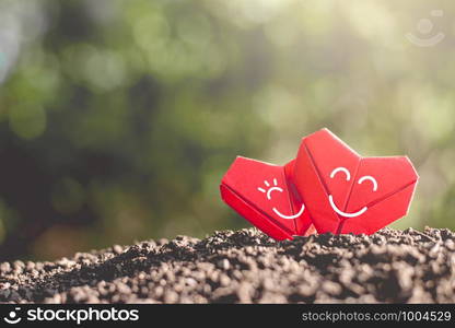 Valentine's Day background with red paper folded in two hearts, placed on the rich soil with morning sunlight shining.