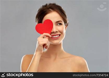 valentine&rsquo;s day, beauty and people concept - happy smiling beautiful young woman covering one eye by red heart over grey background. beautiful smiling woman holding red heart