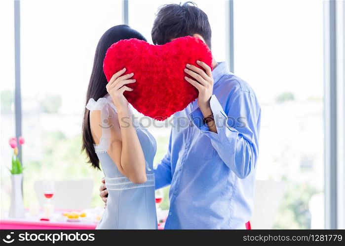 Valentine&rsquo;s day concept,asian Young happy sweet couple in love holding a red heart shaped pillow After lunch In a restaurant background